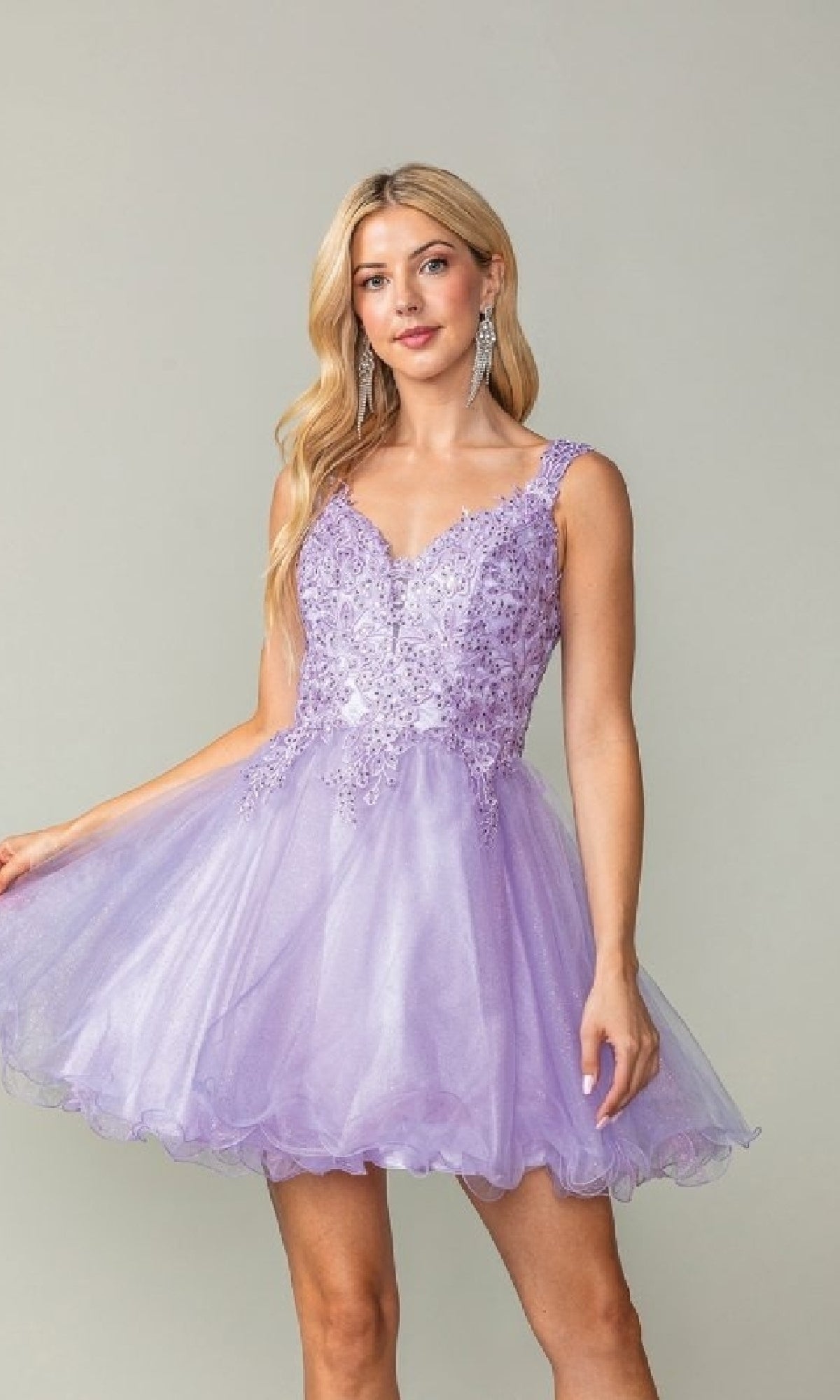Woman wearing a short poofy lilac purple dress with lace details on a plain background